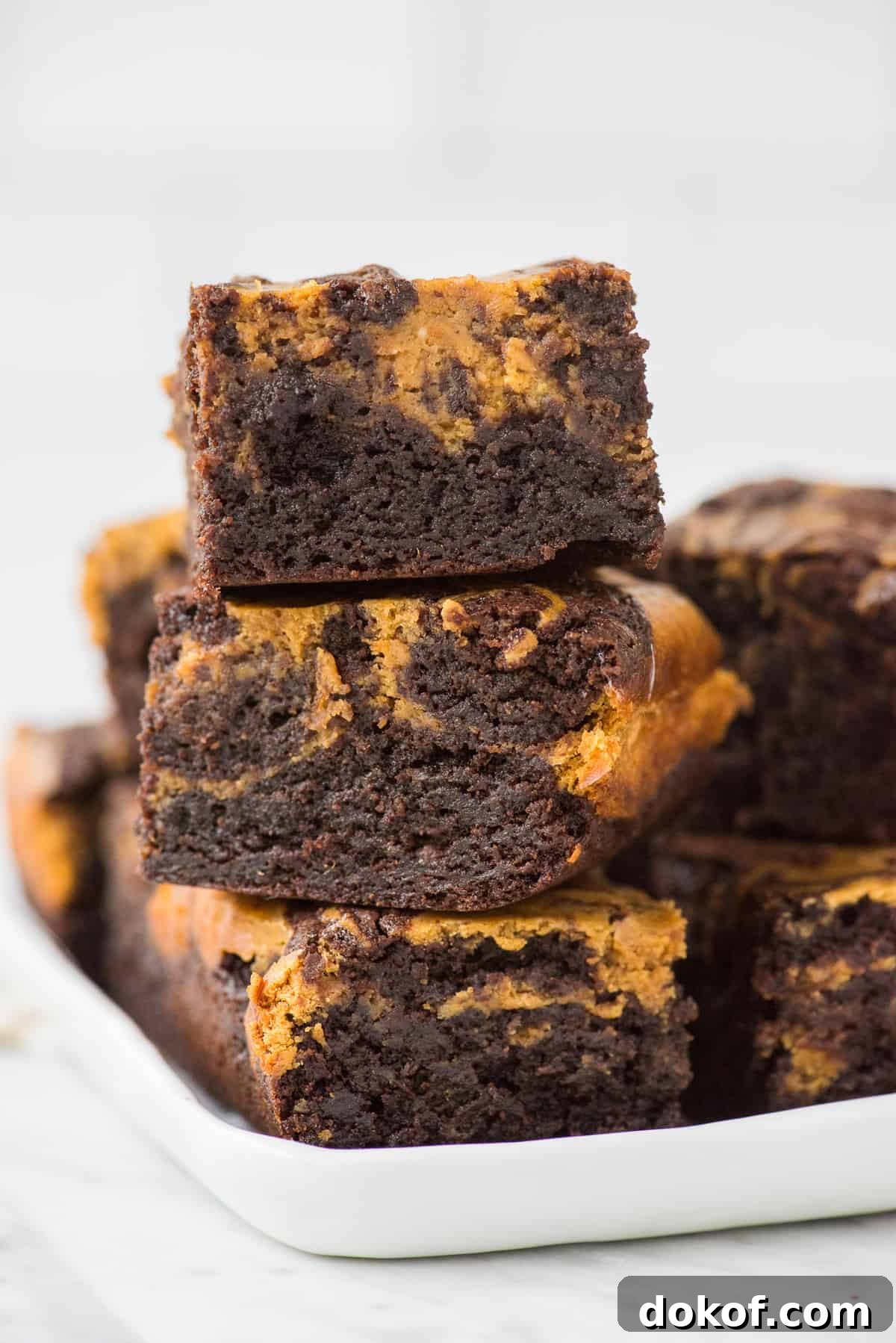 3 pumpkin cheesecake brownies stacked on top of each other on a white tray