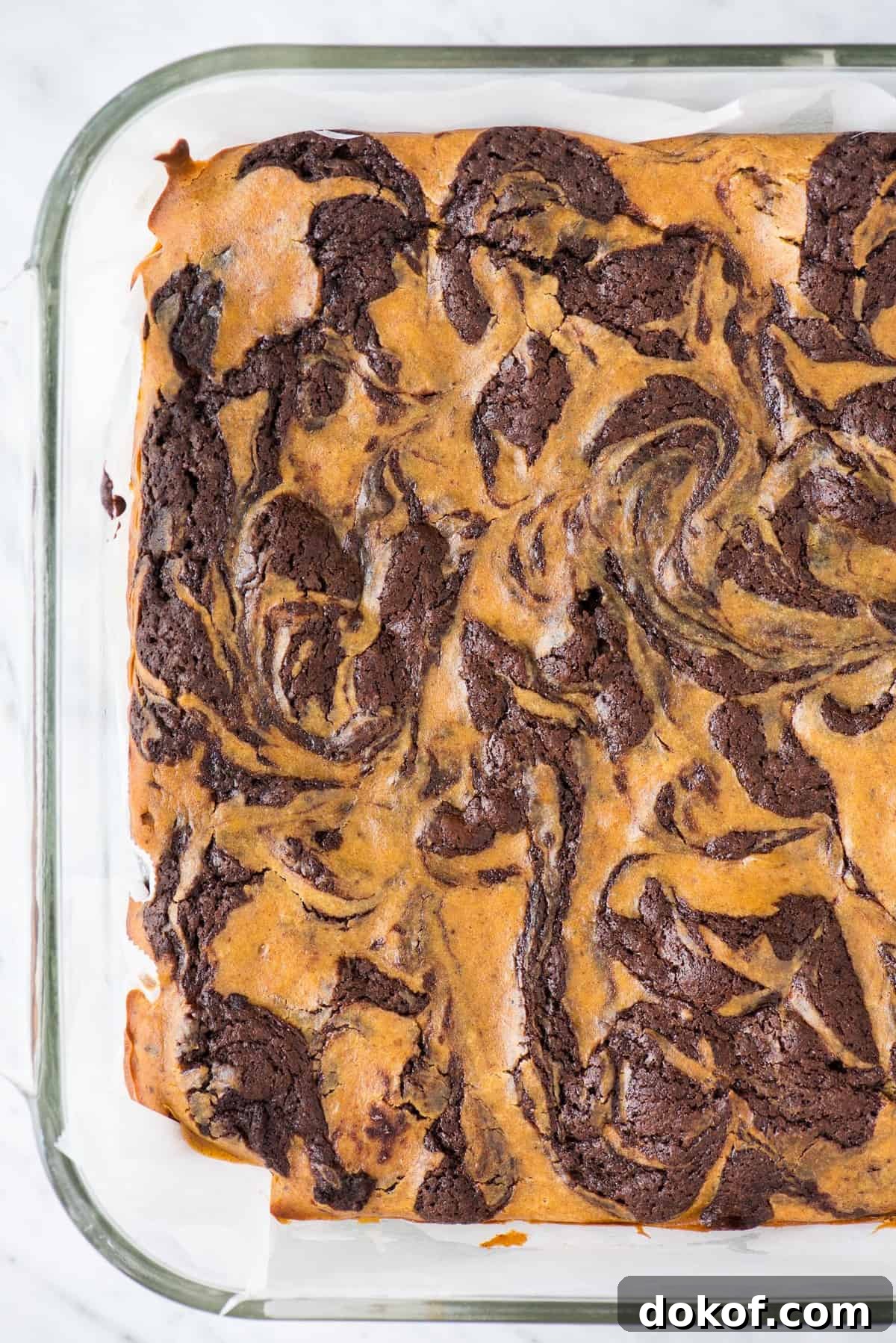 pumpkin swirled cheesecake brownies in glass pan on white background
