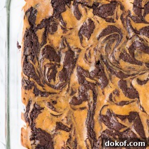 A glass baking dish filled with pumpkin cheesecake brownies, swirled with chocolate and pumpkin for a marbled pattern.