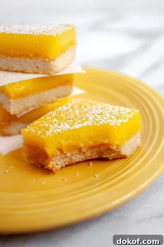 Yellow plate with four lemon bars sprinkled with powdered sugar, one with a bite take out of it.