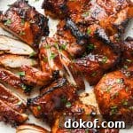 A large white ceramic plate of boneless skinless bbq chicken thighs topped with chopped parsley.