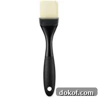 A black-handled silicone pastry brush with white bristles.
