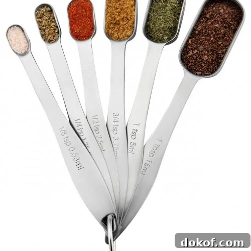 A set of six metal measuring spoons, each filled with a different spice or herb.