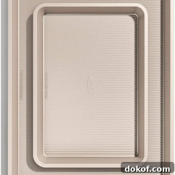 Two beige, non-stick baking sheets of two sizes are stacked inside each other.