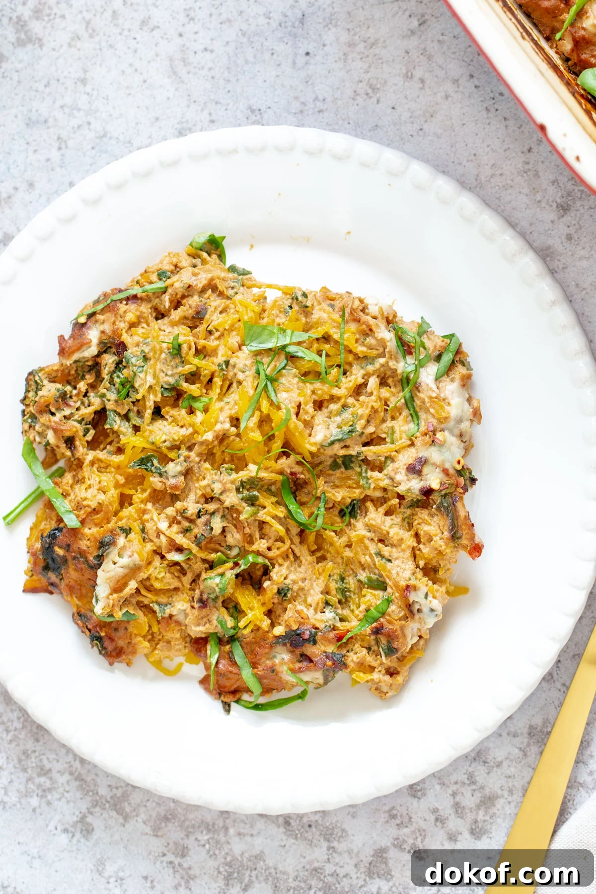 a serving of vegan spaghetti squash pasta bake on a white plate with a golden fork 