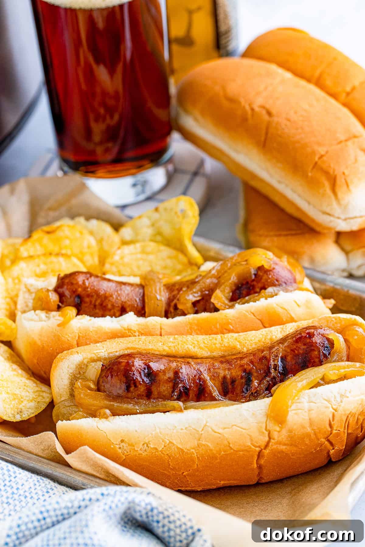Slow cooker beer brats piled on a bun and topped with caramelized onions.