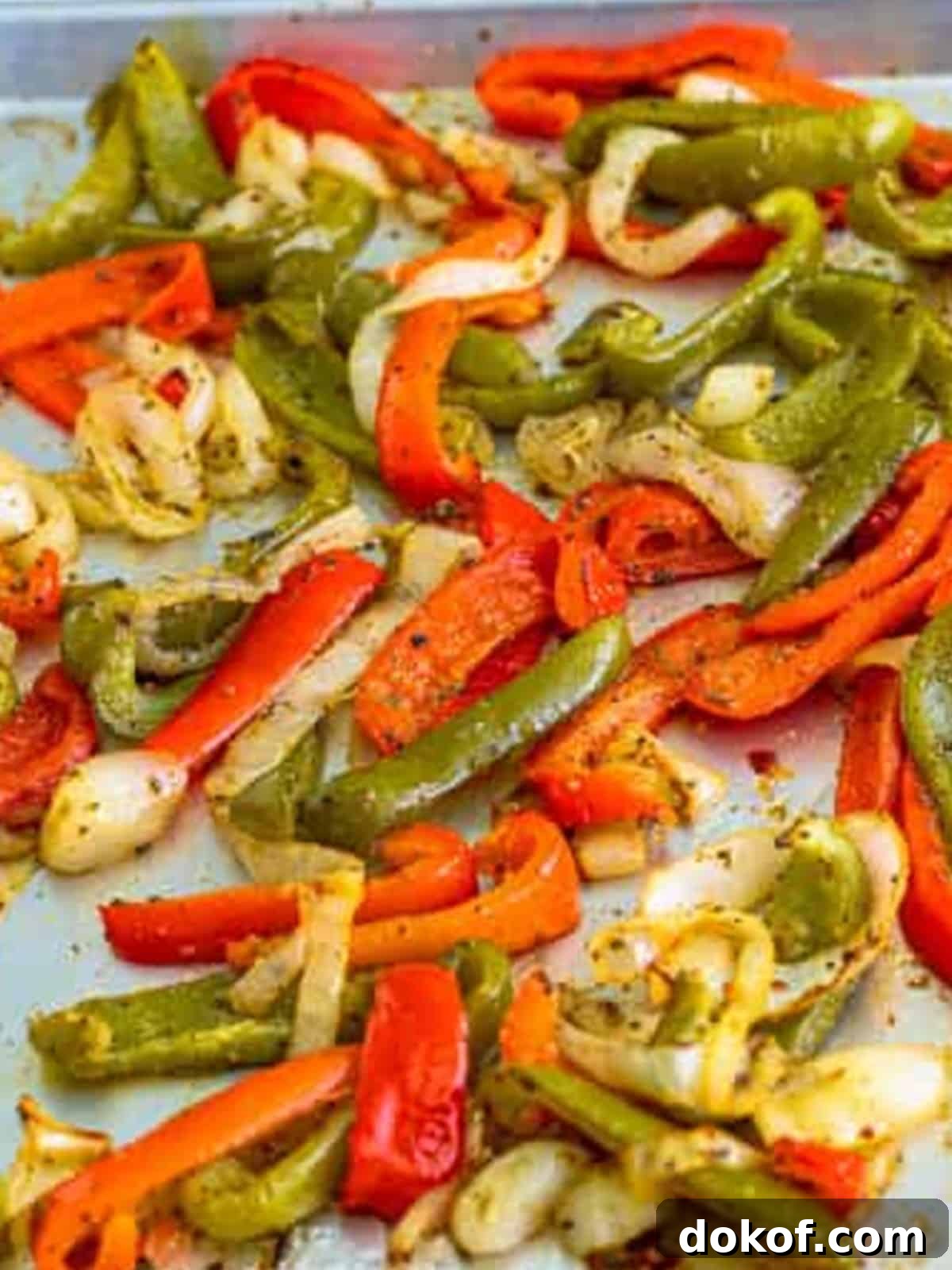 Sliced bell peppers and onions roasted on a sheet pan for Italian sausage sandwiches.