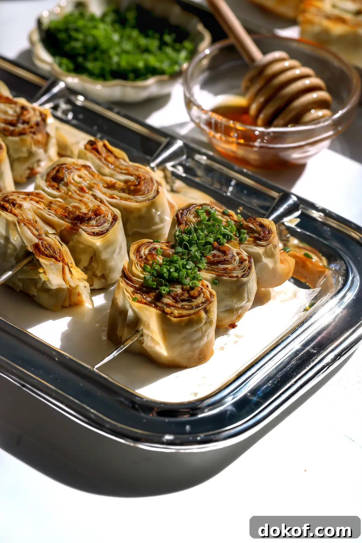 Angled shot of crispy phyllo appetizer skewers served with a side of honey and a wooden dipper.