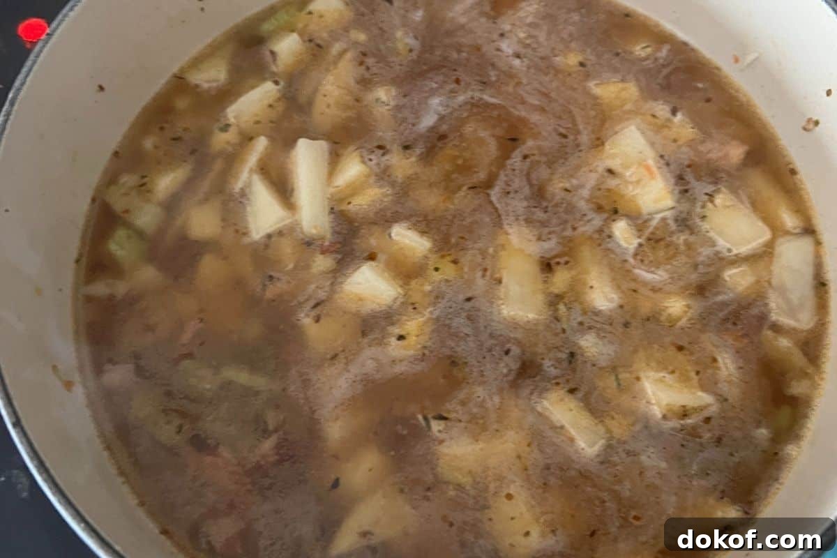 Potatoes cooking with the chicken broth and vegetables on a stovetop.