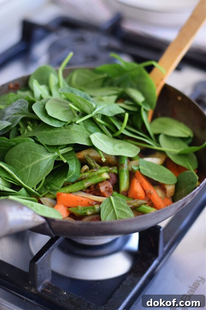 Adding spinach to vegetables in a wok.