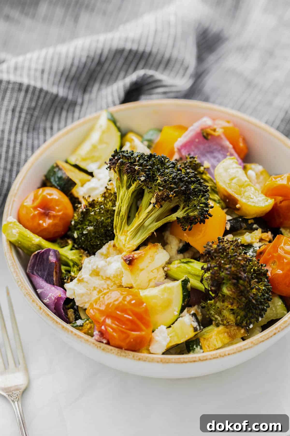 all of the roasted veggies in a bowl with feta