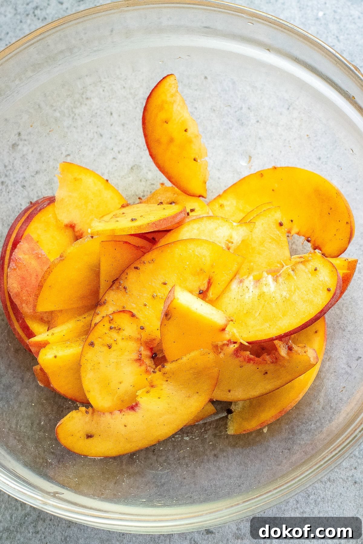 Flaky Peach Puff Pastry Tart Recipe for Summer Dessert 5 An overhead image of sliced peaches coated with brown sugar, cinnamon, and vanilla extract in a bowl.
