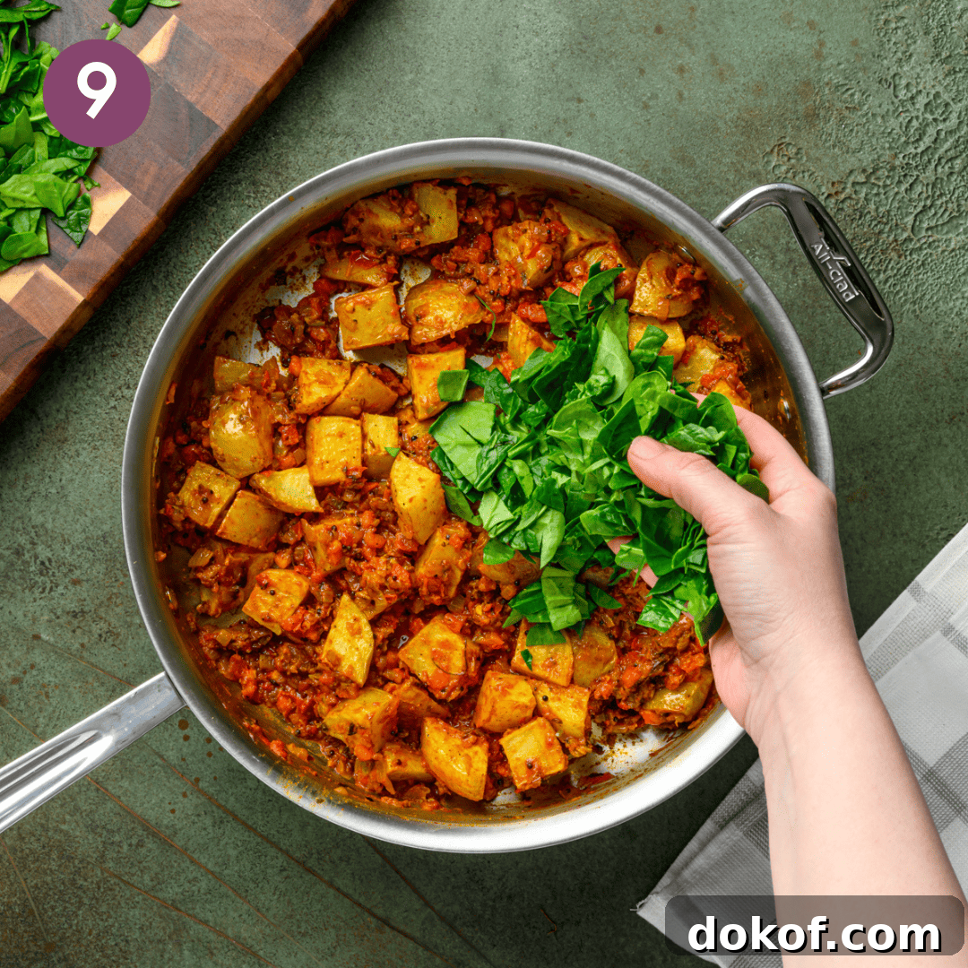 person adding baby spinach to the masala in the pan.