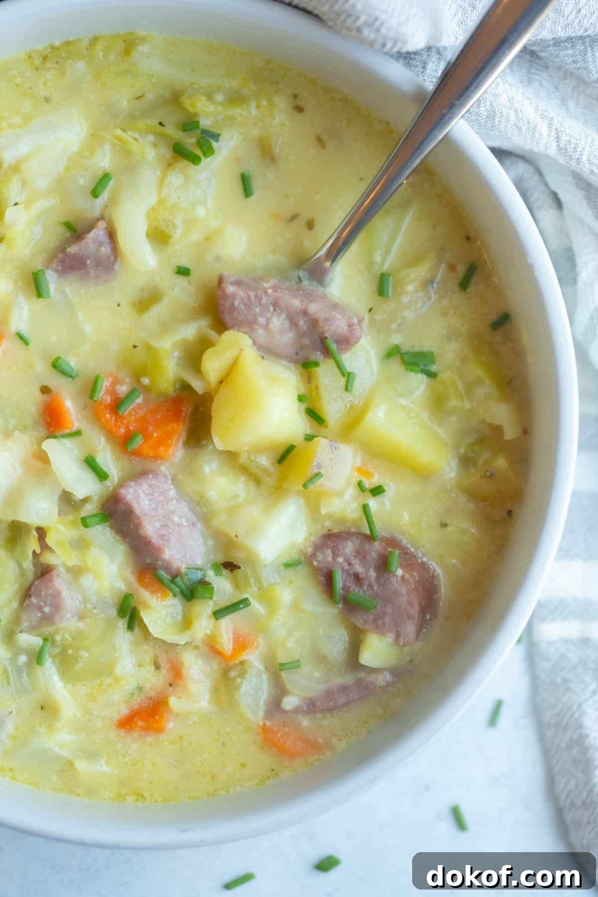 Kielbasa Cabbage Soup in a white bowl with a silver spoon in it.