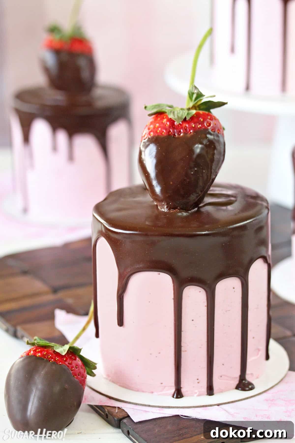 Close-up of mini cake with pink strawberry buttercream, a chocolate drip, and a large chocolate strawberry on top.