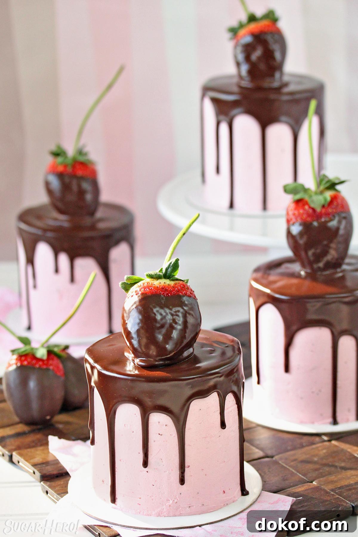 Four mini chocolate cakes, covered with strawberry buttercream, a chocolate drip, and a chocolate-dipped strawberry on top.