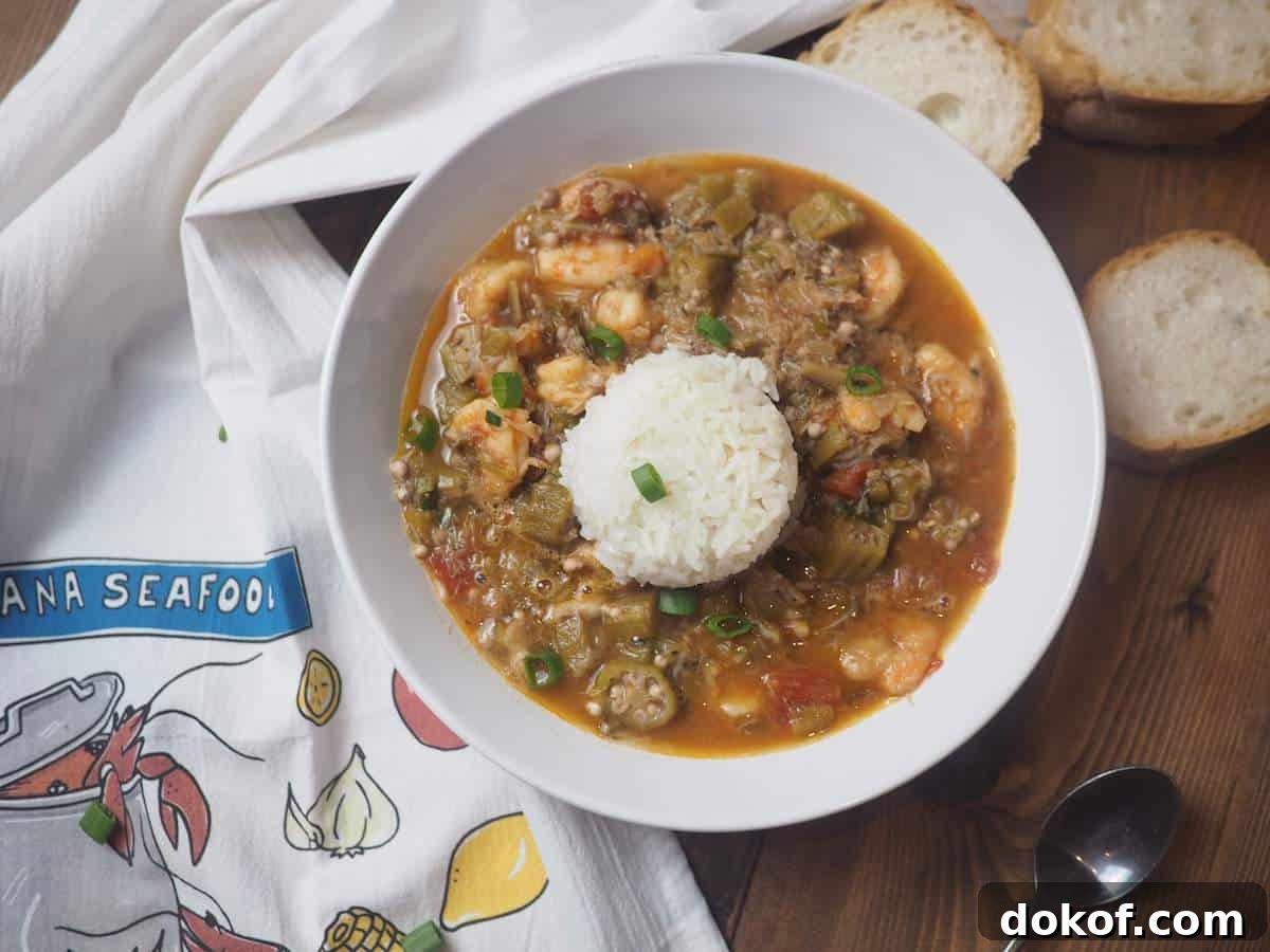 A white bowl of shrimp and crab seafood gumbo with rice and green onions.