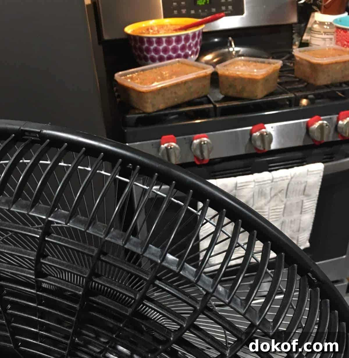 A fan blowing cool air at a bunch of bowls of gumbo on a stovetop.