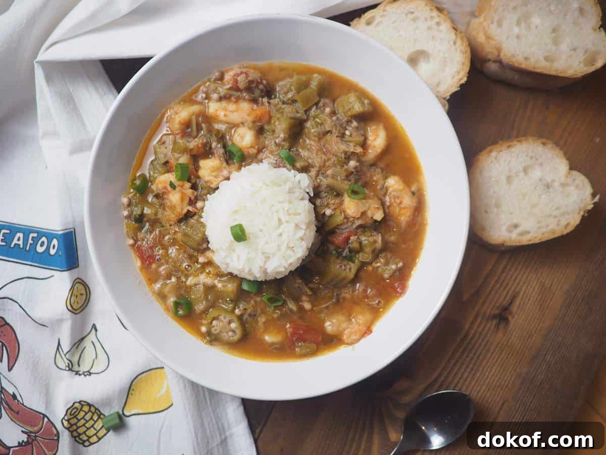 A white bowl of shrimp and crab seafood gumbo with rice, green onions, and french bread.