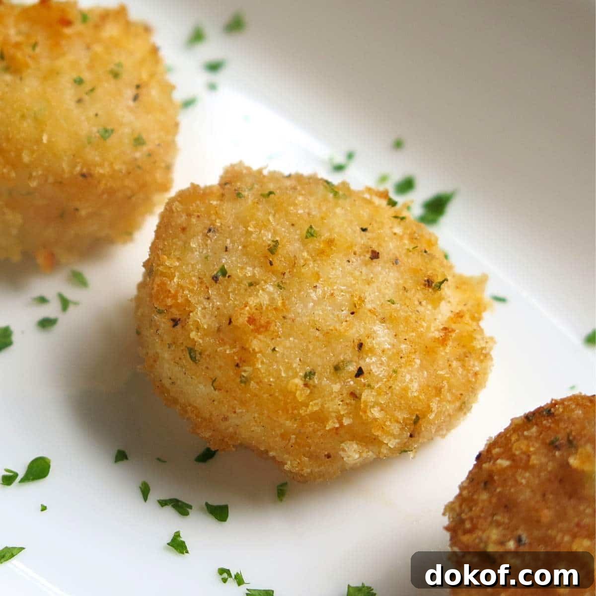 Parmesan Crusted Broiled Scallops lined up on a plate with minced parsley around them.