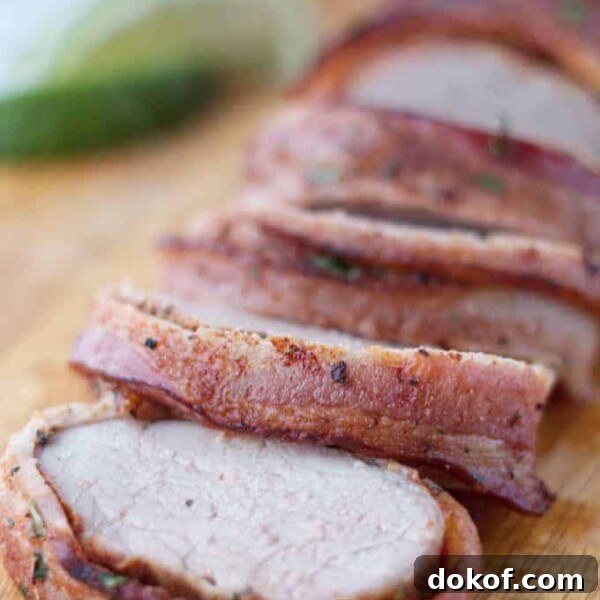Bacon wrapped pork tenderloin cut into slices on wood cutting board with cilantro and lime garnish
