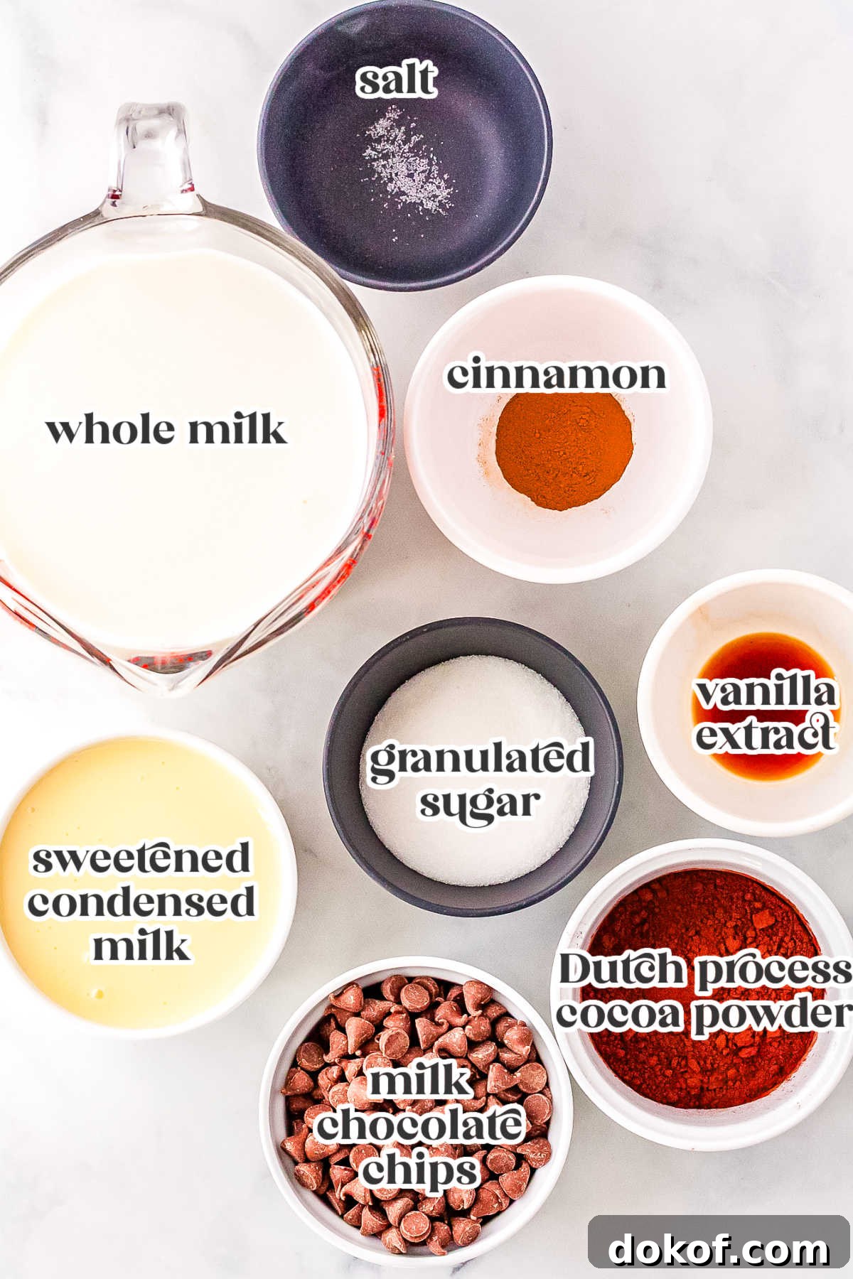 Cozy Cinnamon Hot Chocolate Recipe for Warm Winter Nights 4 Overhead view of ingredients for Cinnamon Hot Chocolate, including whole milk, cocoa powder, sugar, chocolate chips, sweetened condensed milk, cinnamon, vanilla, and salt arranged in bowls.