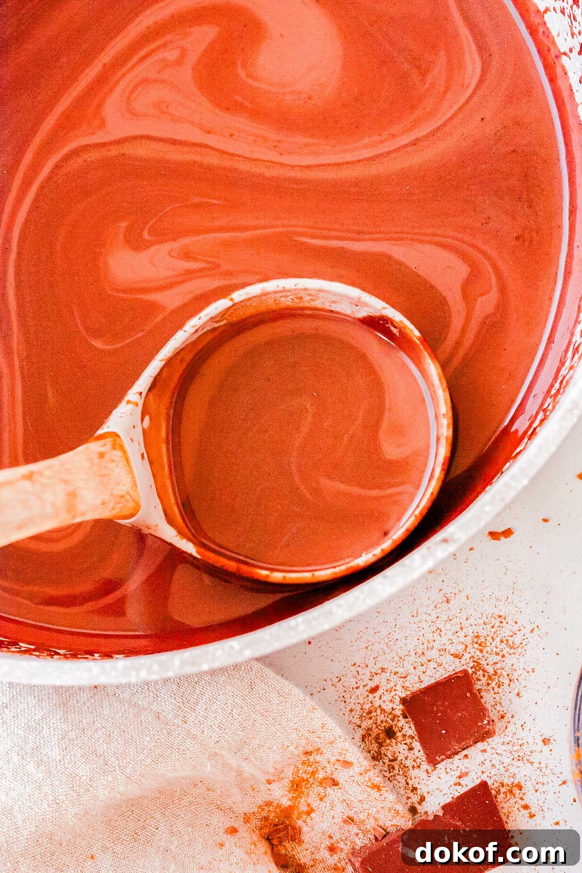 Cozy Cinnamon Hot Chocolate Recipe for Warm Winter Nights 7 Wooden ladle scooping creamy Cinnamon Hot Chocolate from a pot with swirls of melted chocolate on the surface.