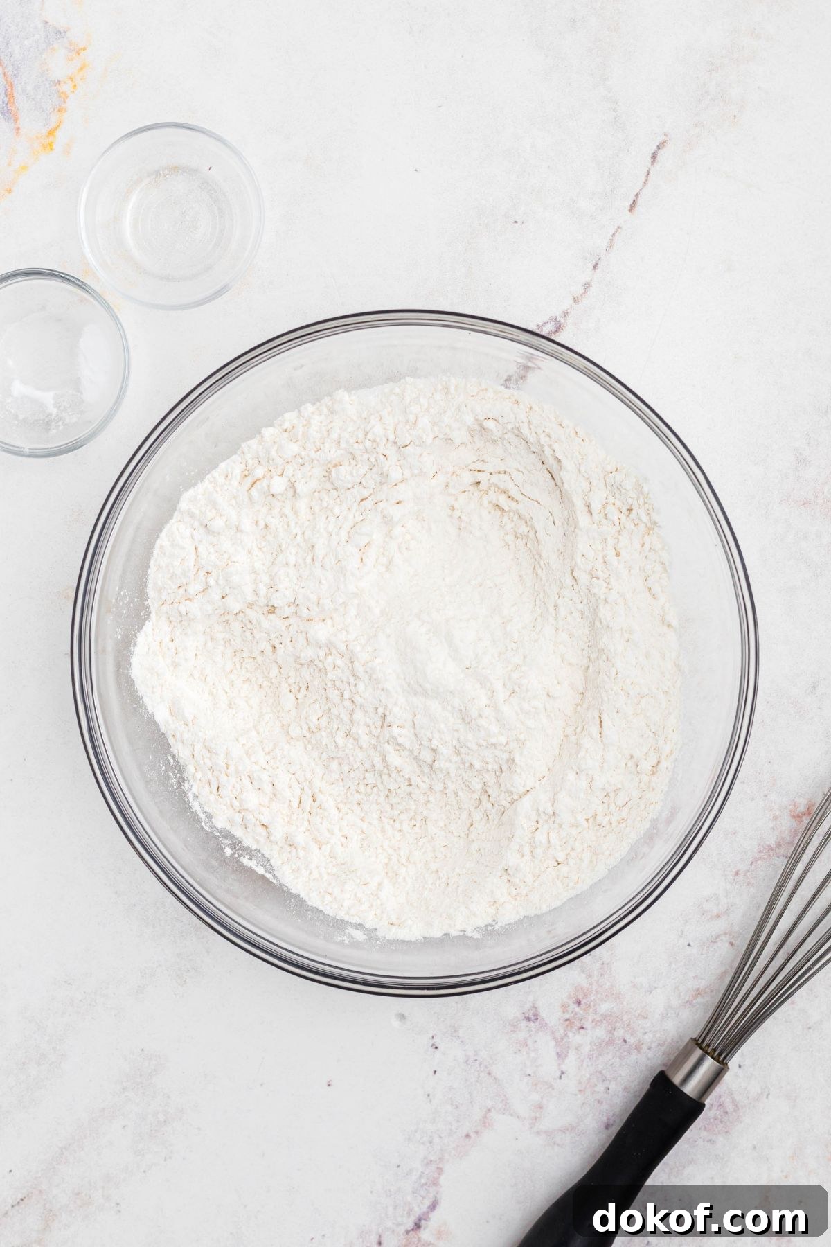 Flour and other ingredients combined in a clear glass bowl. 