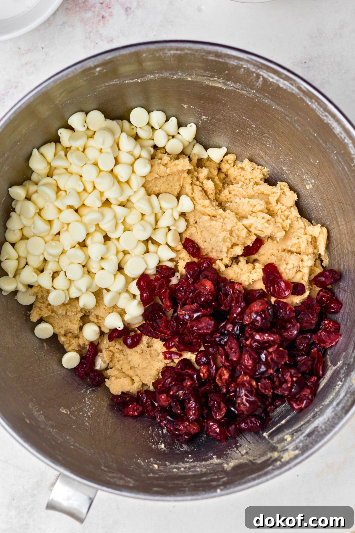 Cranberries, chips, and dough being mixed together in a large silver bowl. 