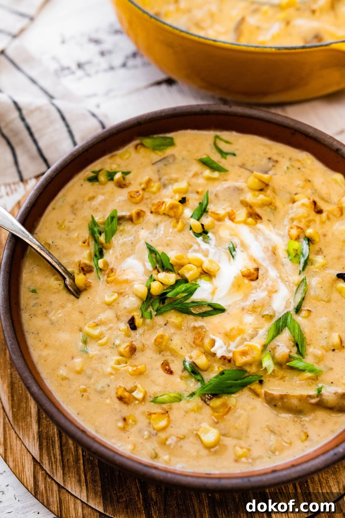bowl of potato corn chowder recipe with sour cream and green onions on top ready to eat. Spoon in the bowl.