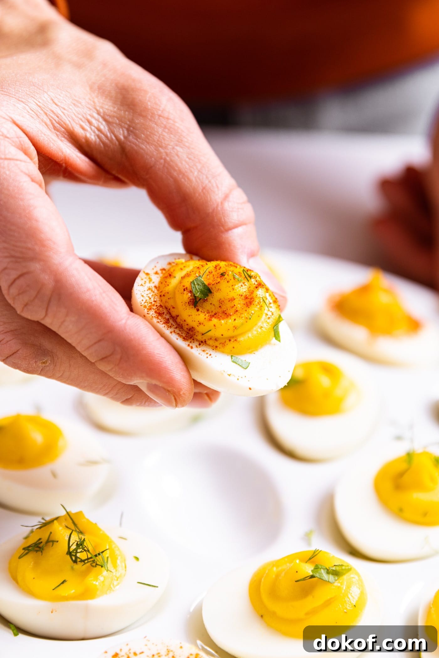 Hand holding half of white deviled egg filled with yellow colored creamy texture and topped with paprika powder