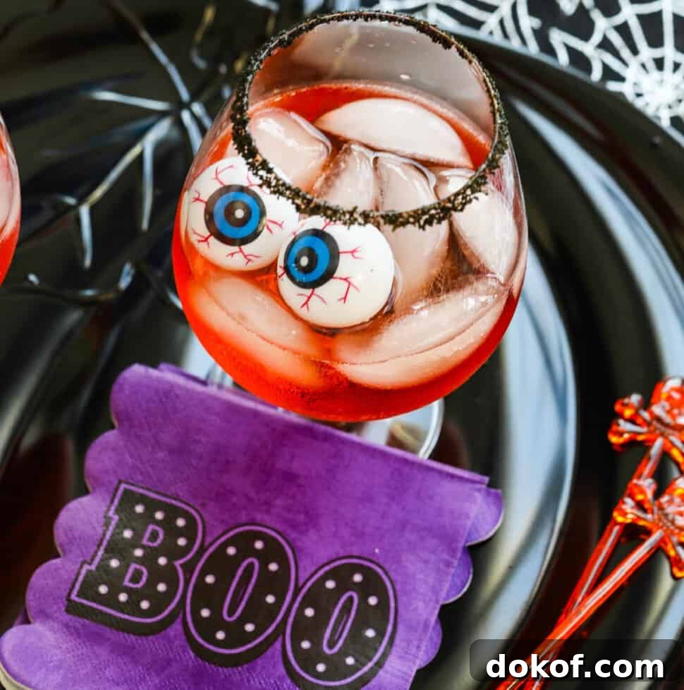 A large cocktail glass with black sugar rim, ice, Aperol cocktail, and eyeballs for Halloween.
