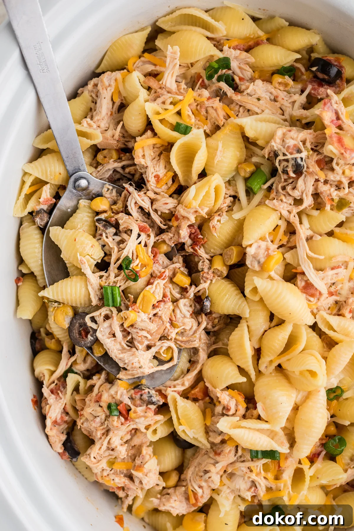 Southwestern Cheesy Chicken Pasta Bake with Roasted Corn and Peppers 2 scooping some southwestern cheesy chicken pasta out of a crockpot.