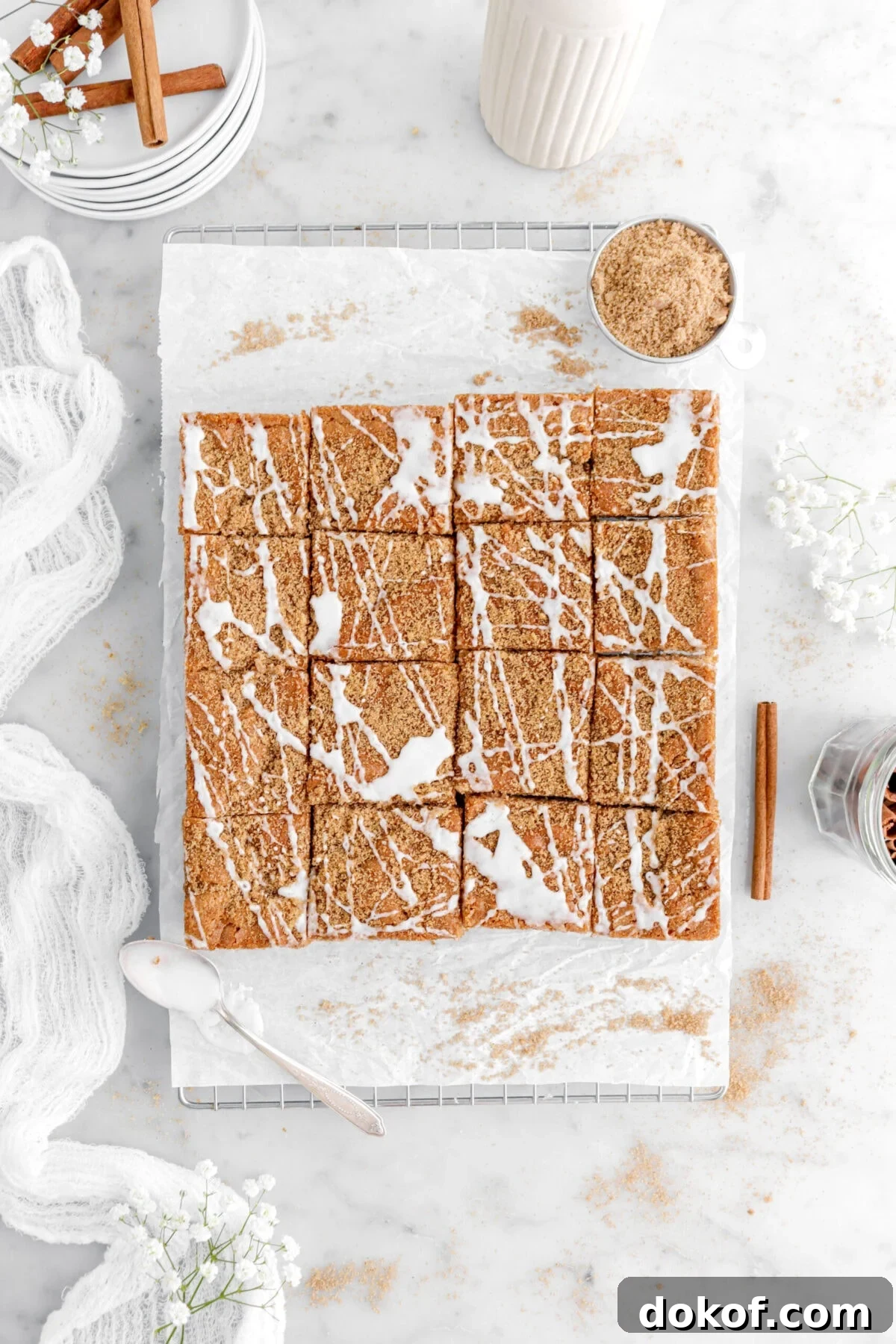 iced blondies on parchment lined cooling rack with a bowl of cinnamon sugar, and a spoon of icing beside.