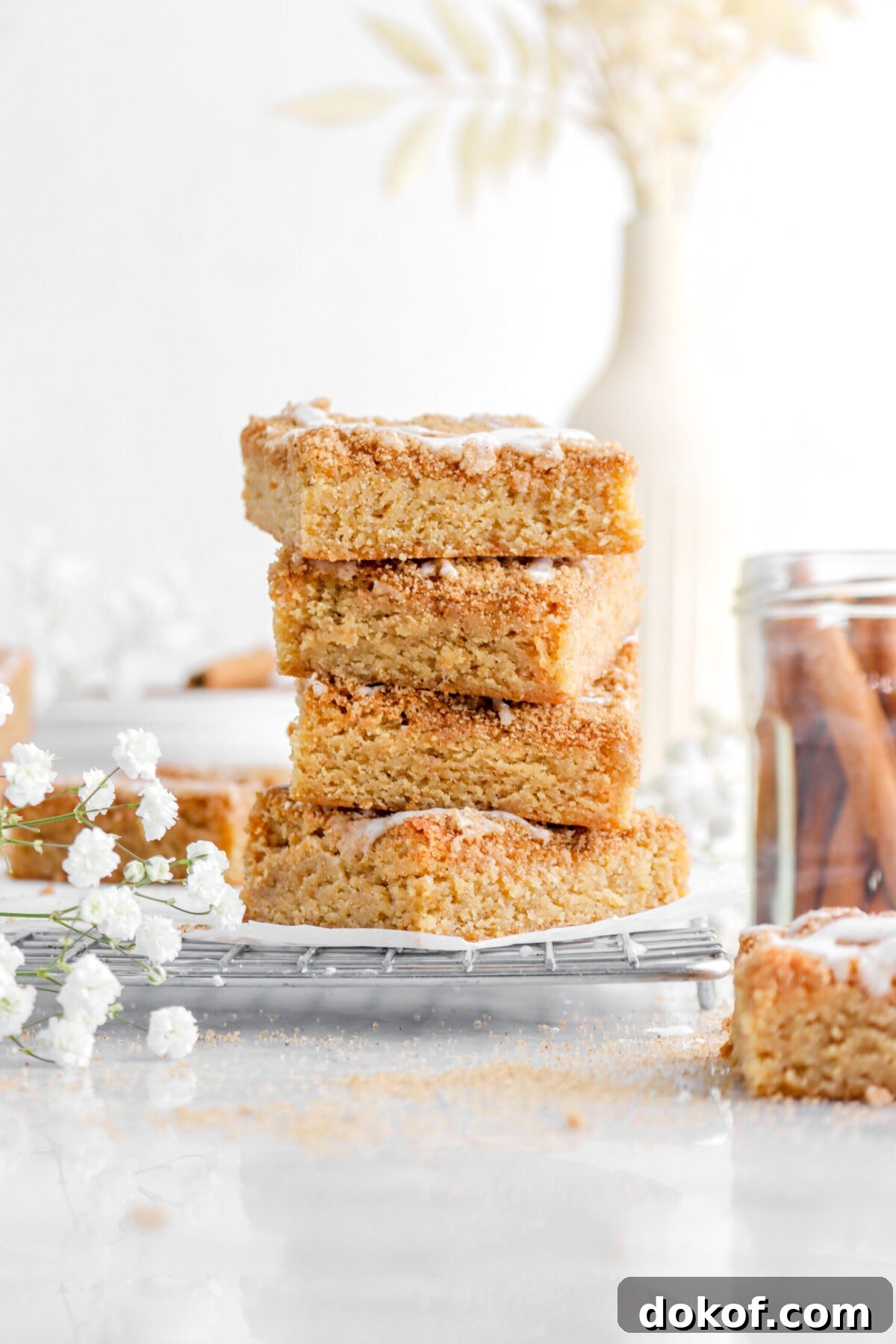 front shot of stacked cinnamon roll blondies with white flowers beside and vase behind.