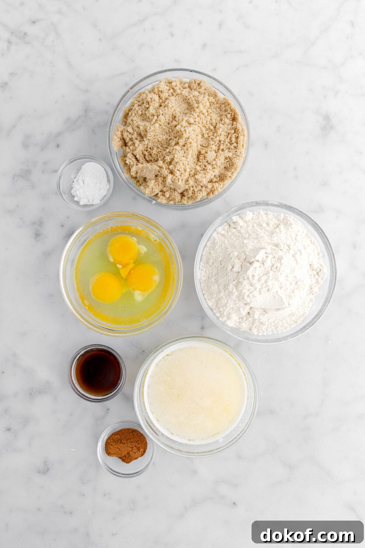 brown sugar, baking powder, eggs, flour, vanilla, melted butter, and cinnamon on marble surface.