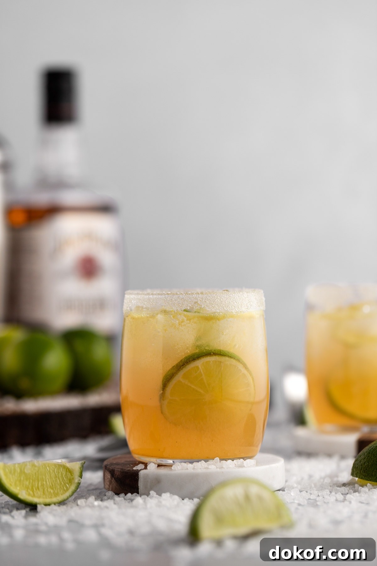Up close view of a whiskey margarita on a marble coaster, with a bottle of whiskey in the background.