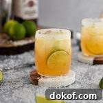 Bourbon margarita on a white and wooden coaster, with a wooden board with limes in the background.