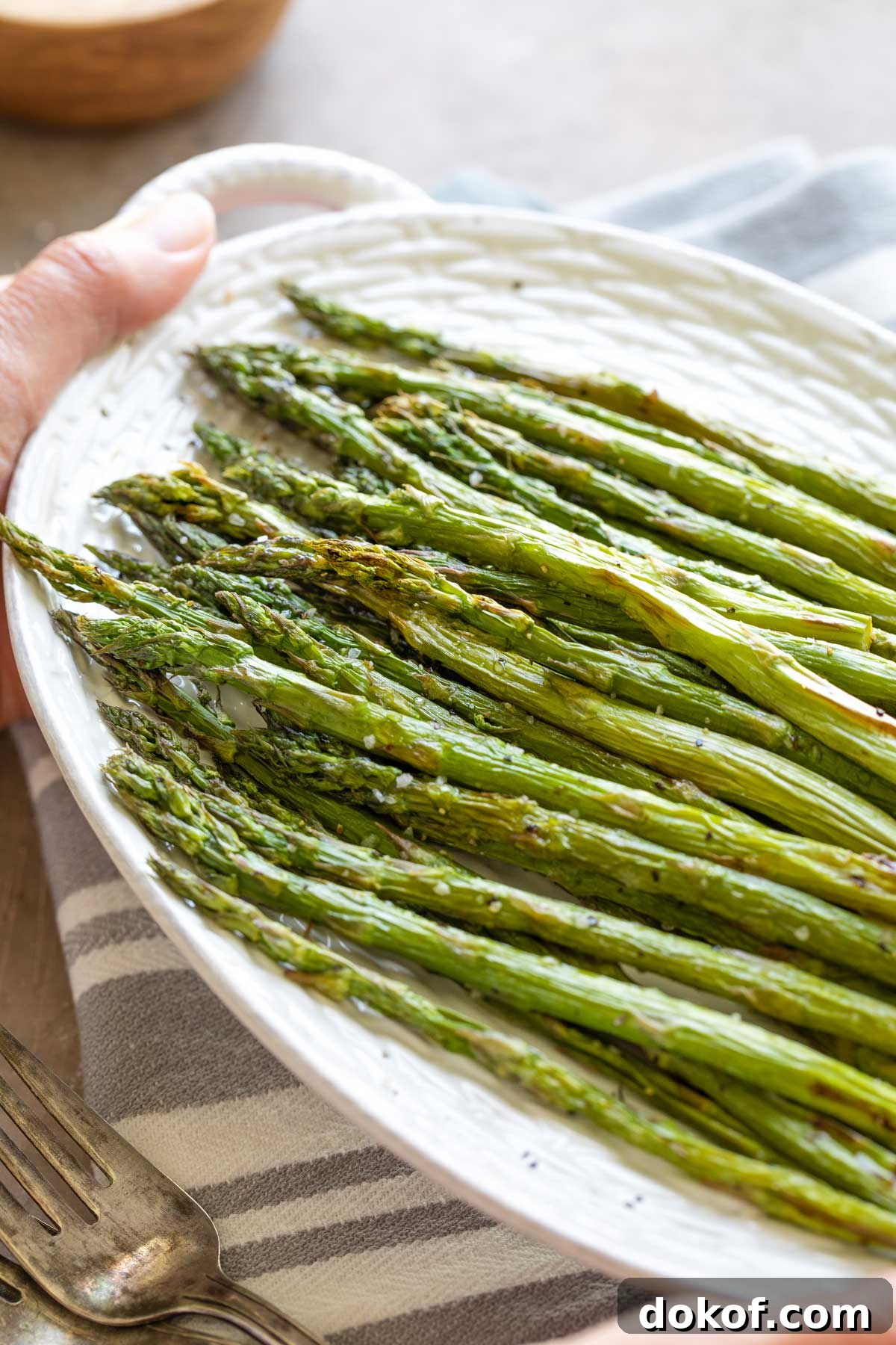 Hands holding serving platter of asparagus above gray-striped cloth.