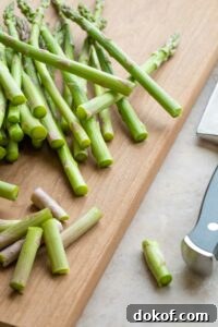 Pile of raw asparagus on cutting board with ends cut off.