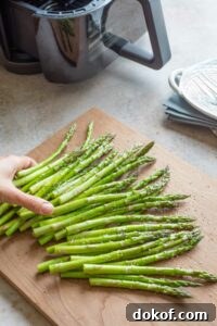 Hand tossing raw asparagus with oil.