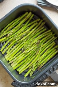 Raw asparagus in single layer in air fryer basket.
