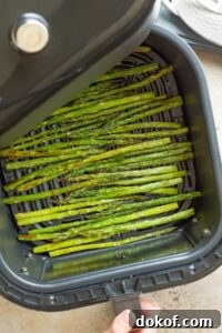 Hand pulling open air fryer drawer with cooked asparagus.