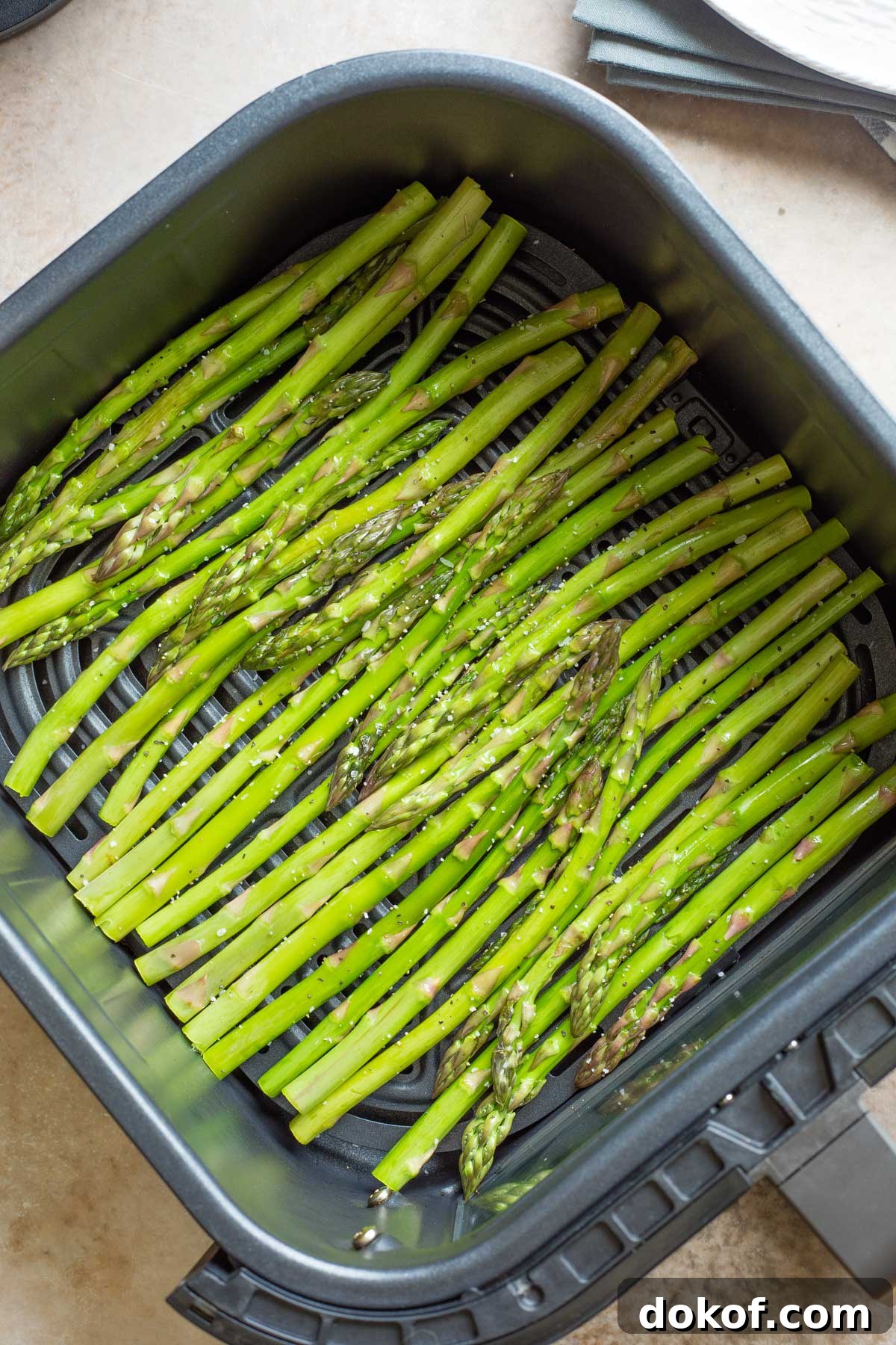 Raw asparagus laid in single layer in air fryer basket.