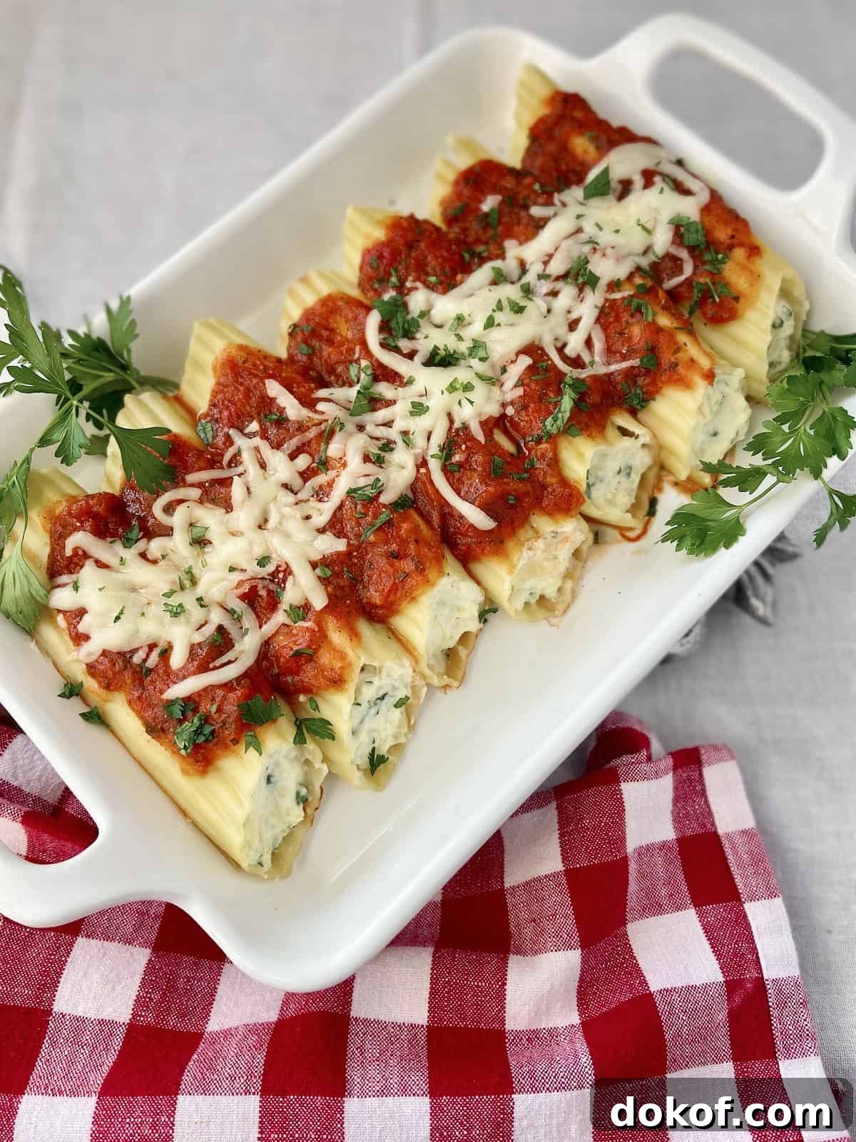 Stuffed Manicotti shells in white baking dish with red sauce on top.