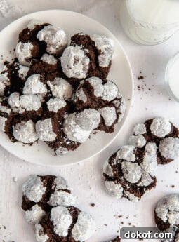chocolate crinkle cookies on white round plate next to more cookies and glass of milk