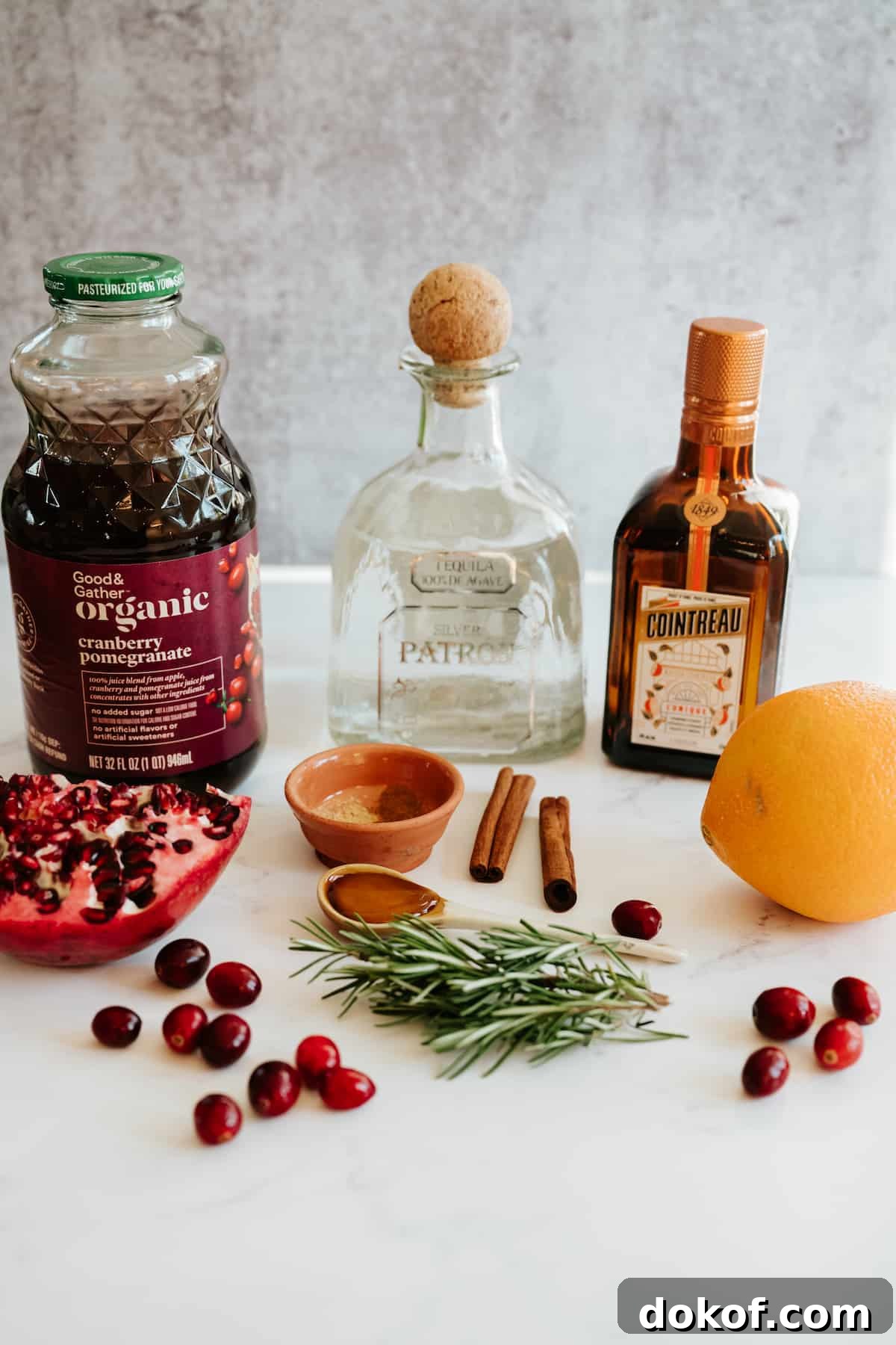 ingredients needed to make a spiced pomegranate cranberry holiday margarita on a white marble bar.