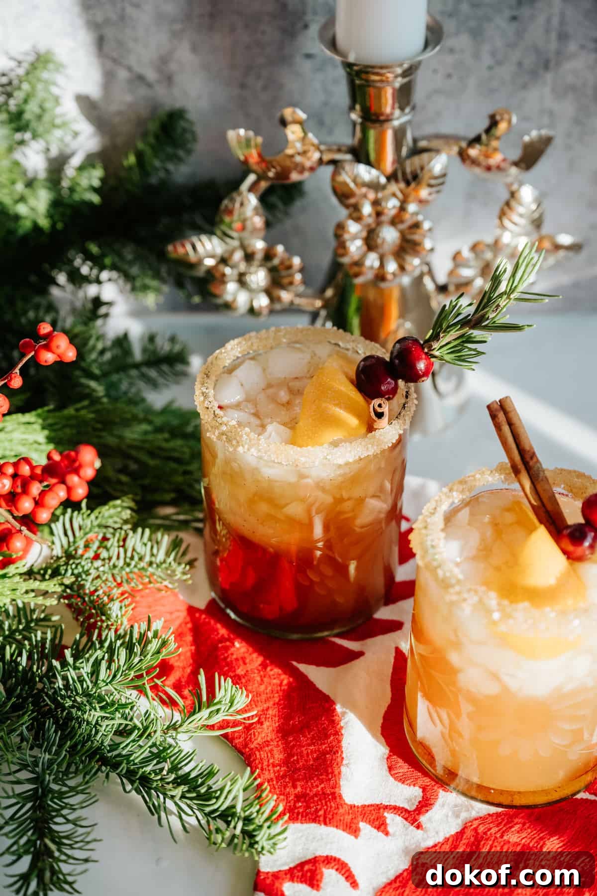 festive holiday table with evergreens and red berries with two spiced pomegranate cranberry margaritas. 