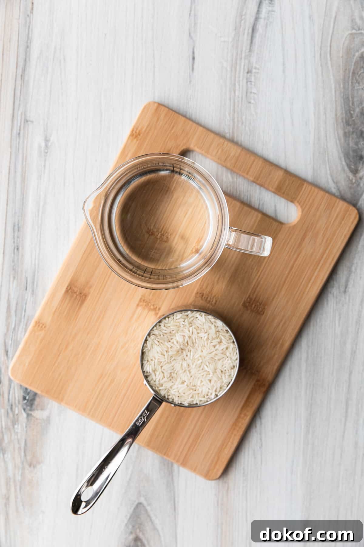 a cup of dry rice and a cup of water on a cutting board