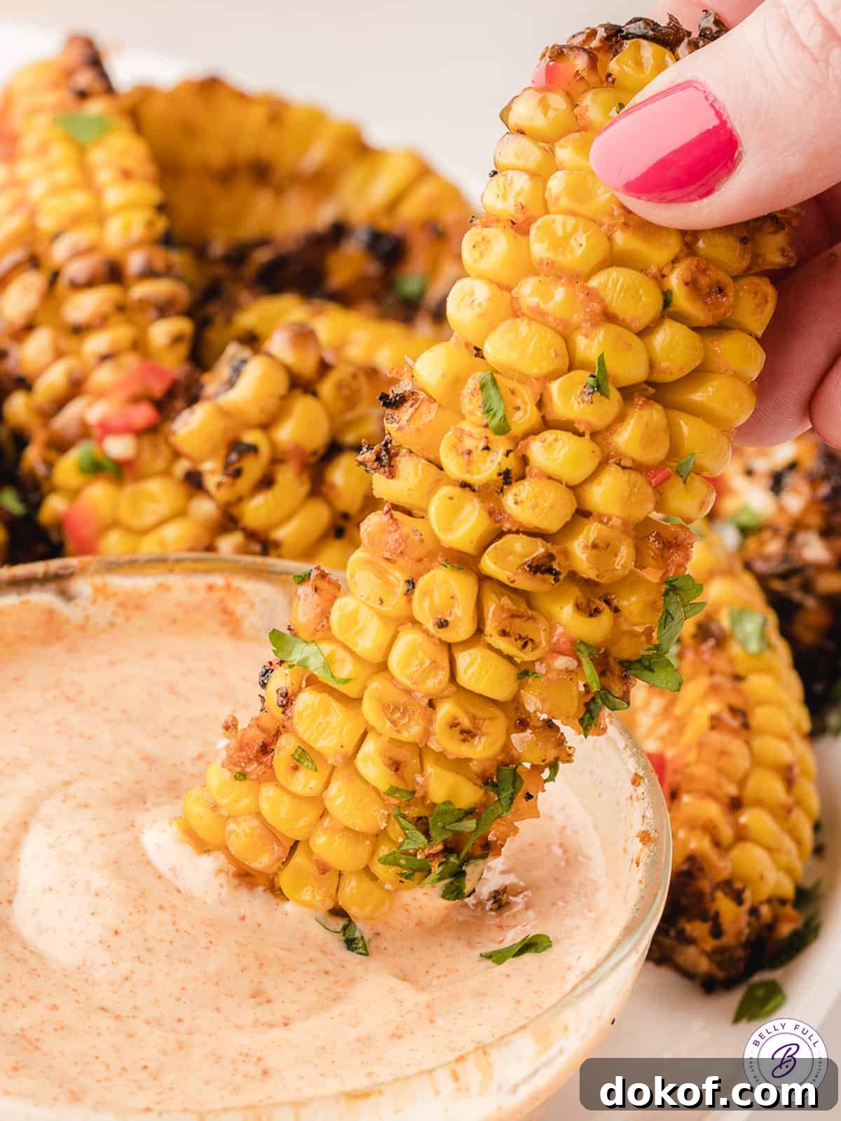 A hand dipping a corn rib into a mayo dipping sauce